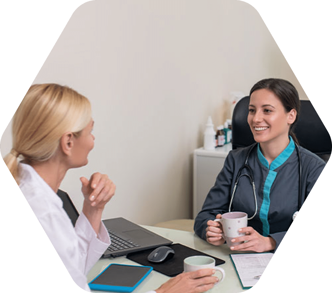 Two female doctors chatting and smiling over coffee in an office.