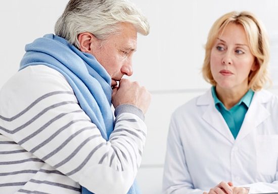 Doctor listening to an elderly man coughing during a consultation.