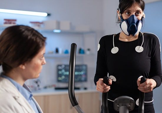 Woman undergoing a cardio stress test with mask and sensors on exercise equipment.