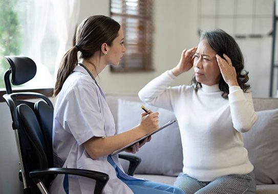 Nurse taking notes while elderly woman describes a headache.