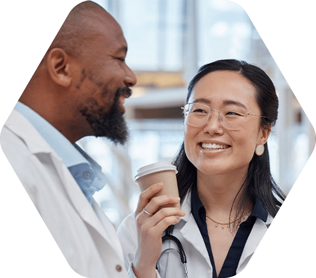 Two doctors smiling and talking, one holding a coffee cup.