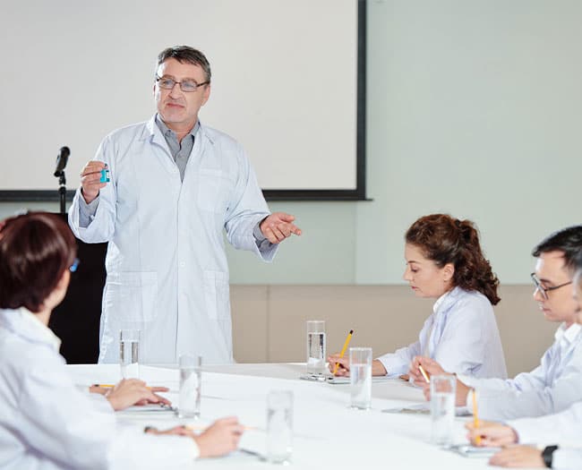 Doctor presenting a medication bottle to colleagues during a meeting.