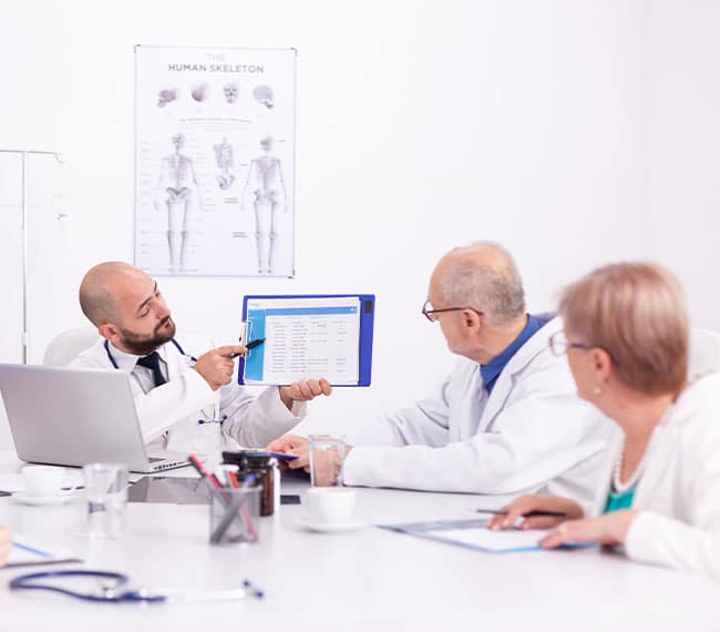 our-sites-01 Doctor presenting medical data to colleagues during a meeting.